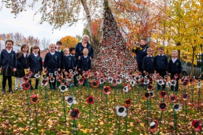 Children and two adults standing outside next to poppy display