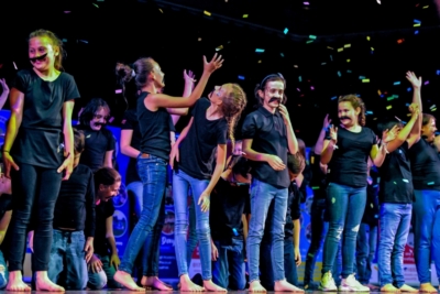 Student on stage wearing matching black t-shirts and blue jeans with confetti falling from the sky