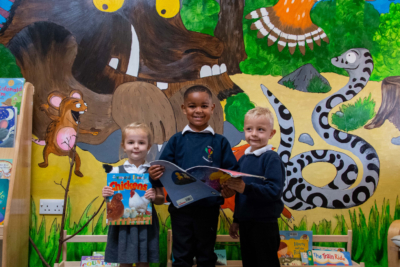 3 young children holding a book standing in front of a Gruffalo wall