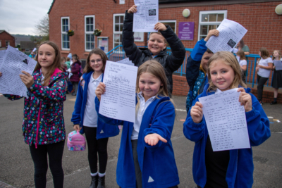 6 school children holding up assignments in a playground