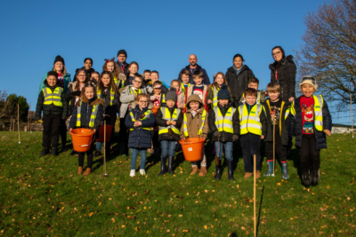 A large group of children and teachers stood in a field after planting trees