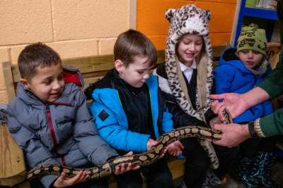 4 children inspecting a snake held by a man