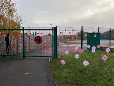 Exterior of a school with green fences covered in Remembrance Ceremony artwork including poppies and a soldier