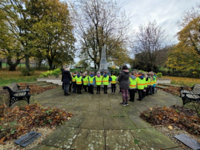 A group of children in high visibility jackets standing in front of a cenotaph
